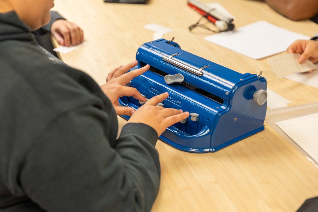 Los estudiantes utilizan una maquinilla especializada en sistema braille para redactar los rótulos.