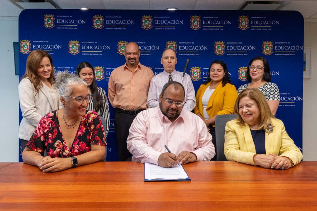 Durante la firma estuvieron presentes (sentados) la Dra. Agnes Bosch Irizarry, en representación de la rectora interina del Recinto de Río Piedras UPR; el Lcdo. Eliezer Ramos Parés, secretario de Educación; y la Dra. Ilka Ríos Reyes, presidenta interina de la UPR. De pie, en el mismo orden: Yasmin Santiago, directora de Programación y Operaciones de AC3; Ariana Rodríguez, estudiante graduada participante de los proyectos de investigación de AC3; el Dr. José Agosto, investigador principal de AC3; el Dr. Manuel Álvarez, líder de Asistencia Tecnológica de AC3; Lizbeth Alvarado, estudiante graduada participante de los proyectos de investigación de AC3; y la Dra. Beverly Morro, subsecretaria para Asuntos Académicos y Programáticos del DE.